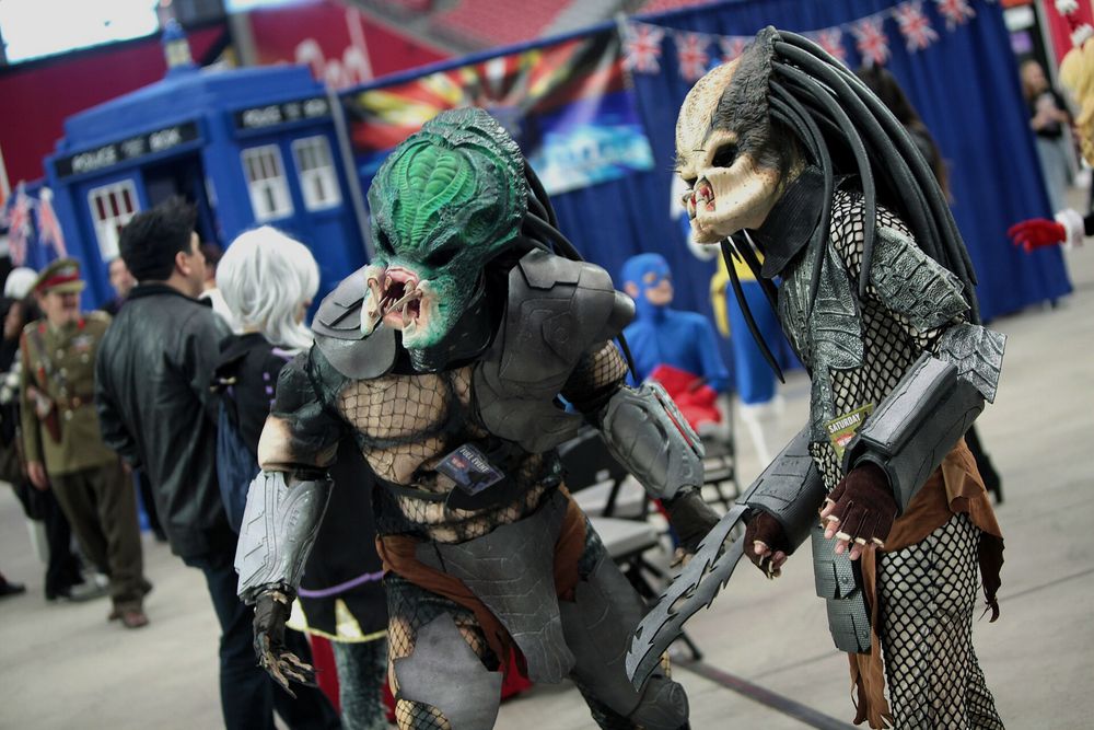 Zwei aufwendige Yautja-Kostüme mit Netzanzug, Schulterpanzer und Klingen auf einer Comic-Messe