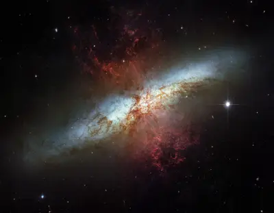 Hubble-Aufnahme der Zigarrengalaxie M82 mit flammenartigen, rötlichen Wasserstoffausflüssen, die senkrecht aus der Scheibe strömen