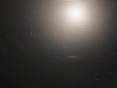 Hubble-Aufnahme der nahezu kreisrunden elliptischen Galaxie M89 als gleichmäßig leuchtender Lichtball vor dunklem Hintergrund